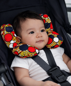 Newborn baby seated in a car seat wearing an AfriBloom wax fabric support pillow, shown in everyday travel setting