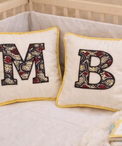 Pair of personalized baby initial cushions with African print appliqué letters placed in nursery crib, handmade decorative pillows for baby room