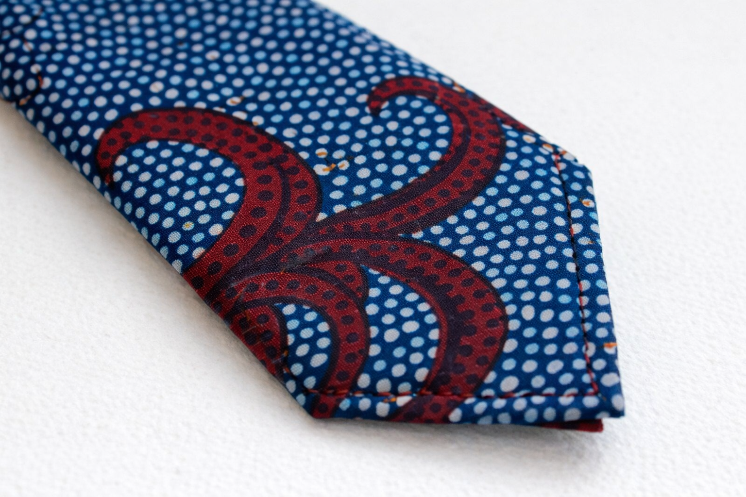 Close-up of AfriBloom handmade African wax print necktie showing stitching, fabric texture, and pointed tip detail, made in Belgium